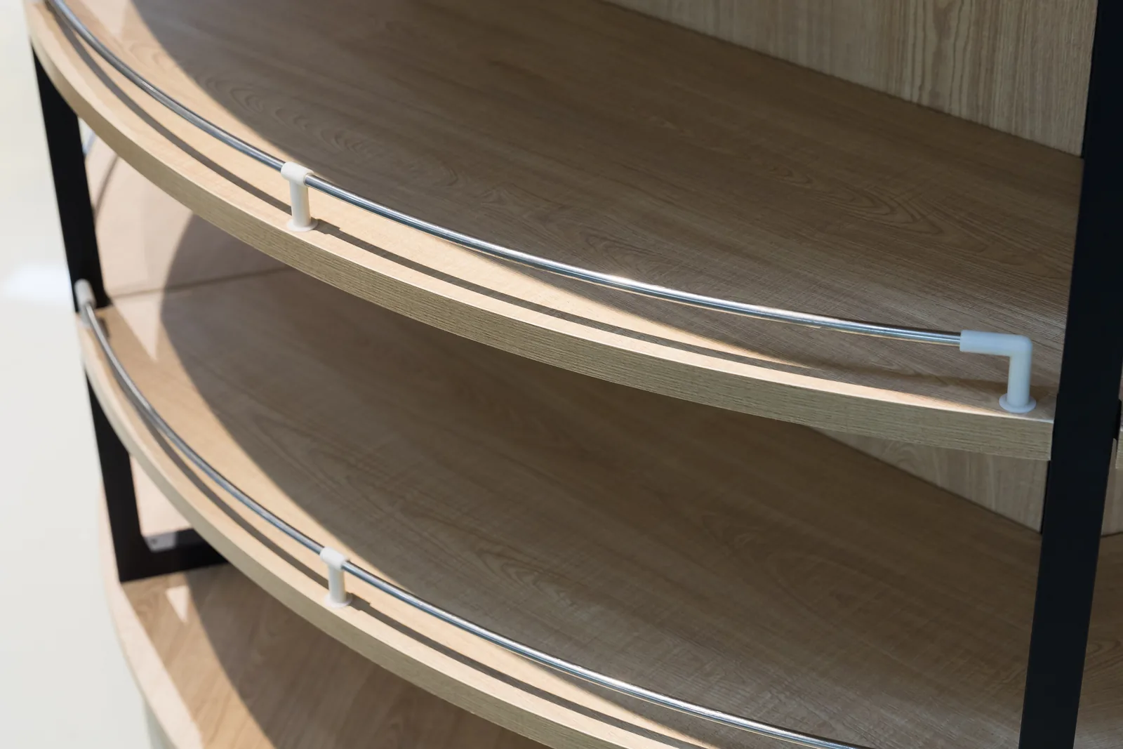 Close view of a curved timber shelf and chrome retaining rail on a Keshun steel and wood display unit