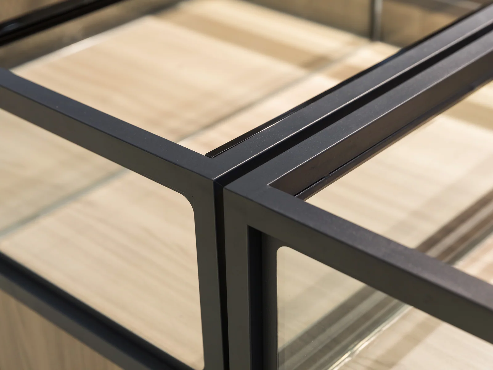 Four sided glazed island cabinet photographed from a corner, showing two glazed faces and the timber base