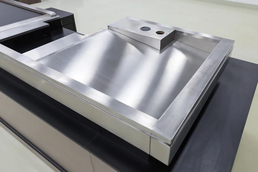 Polished stainless steel top board of a Keshun checkout counter with a welded scan well and cable grommets